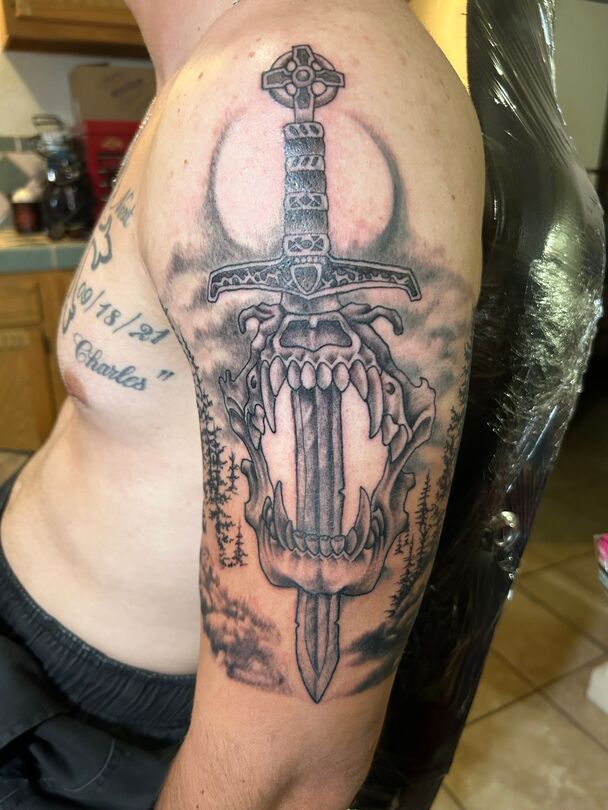 Tattoo on arm: a sword piercing through a skull, with a crescent moon background.