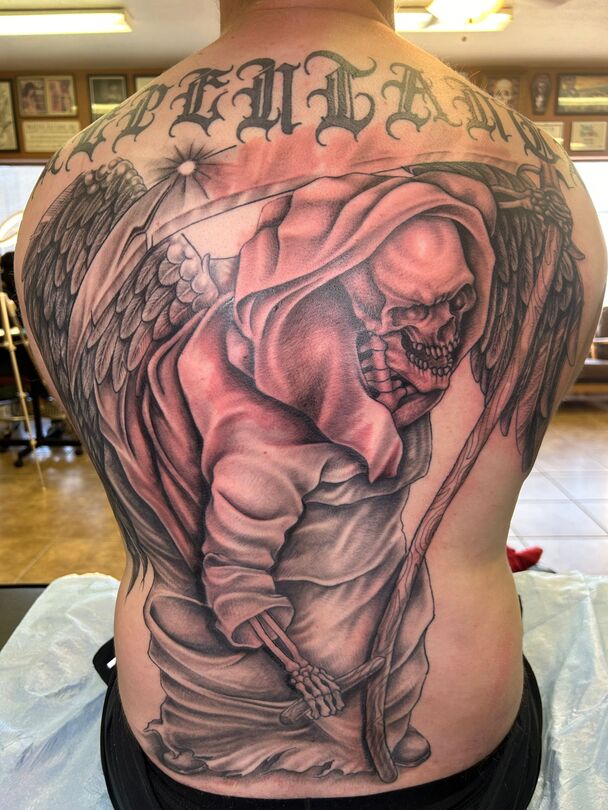 Tattoo on a back depicts Grim Reaper with wings, holding a scythe, and the word