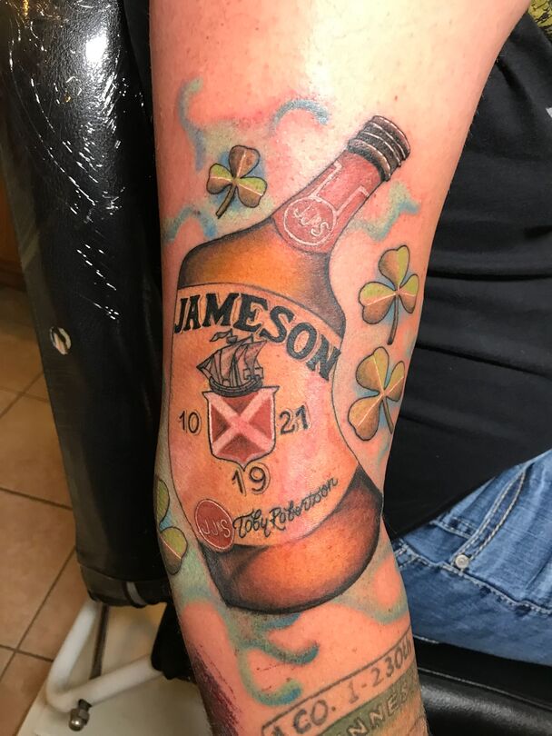 Tattoo of a Jameson whiskey bottle with shamrocks on a person's arm.