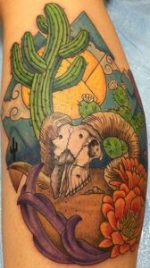 Tattoo of a desert scene with a ram skull, cacti, mountains, and orange flower.