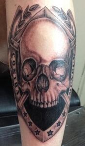 Tattoo of a skull within a shield and laurel leaves; text