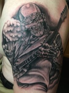 Tattoo of a skeletal figure wearing a metal helmet, playing a guitar, with a mushroom cloud in the background.