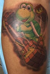 Cartoon Koopa Troopa character tattoo on skin, holding brick blocks, and smiling.