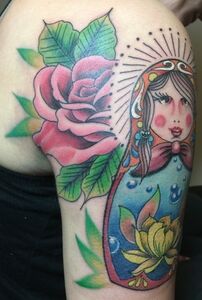 Tattoo on arm of a Russian nesting doll and a pink rose, with green leaves, and a yellow flower.
