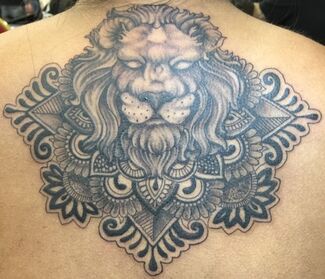 Tattoo of a lion's face with a detailed mandala design on a person's back; grayscale.