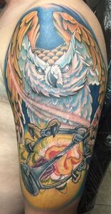 Colorful owl tattoo on a shoulder and upper arm, with wings, an hourglass, and blue/yellow hues.