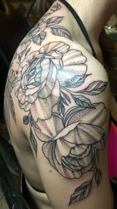Black and white floral tattoo on a person's shoulder, featuring large flowers and leaves.