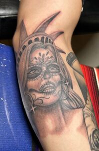Tattoo on arm of Lady Liberty stylized as a sugar skull, in black and gray.
