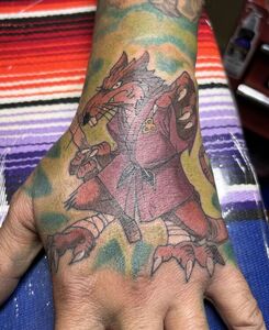 Hand with a tattoo of a rat dressed in purple clothing, holding a sword.