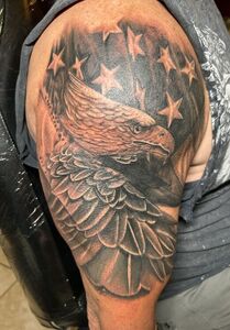 Tattoo of a bald eagle with wings spread, stars, and American flag elements on a shoulder.