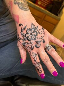 Hand tattoo with a floral design in black ink. The nails are painted bright pink.
