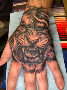 Hand tattoo: Roaring tiger face in black ink.