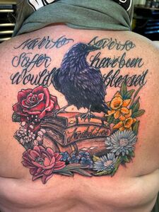 Tattoo of a black raven on books surrounded by flowers; script reads,