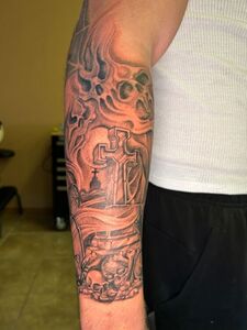Arm tattoo: graveyard scene with cross, skulls, and smoky background.