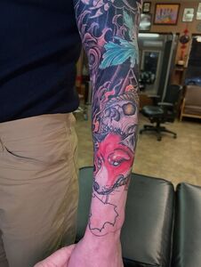 Person's arm with colorful tattoo sleeve featuring a fox, skull, and other designs.