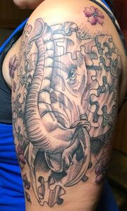 Tattoo of an elephant's head formed by puzzle pieces, shaded in black and gray, with pink flowers.