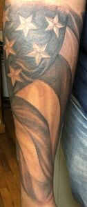 Tattoo of a black and white American flag waving on a person's arm.