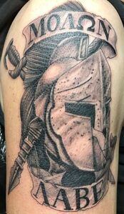 Tattoo on arm. Spartan helmet with sword, Greek text