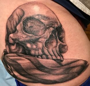 Black and gray skull tattoo on skin, resting on a flowing cloth.