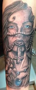 Tattoo of a veiled woman, pearls, a cross, and an ornate cuff with a blue gem. Black and white.