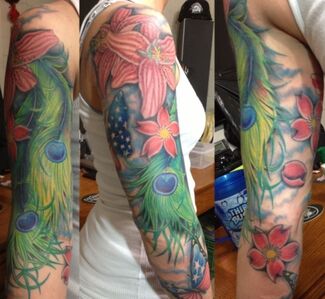 Tattoo of a woman's arm with colorful flowers, peacock feathers, and a partial American flag.