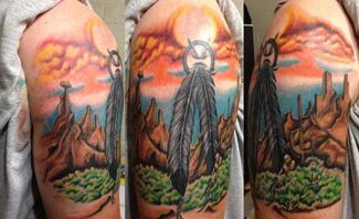 Tattoo of a landscape with feathers and mountains under a colorful sunset.
