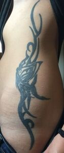 Black tribal tattoo on a person's side, possibly torso, with a floral-like design.
