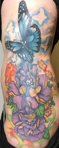 Tattoo of a blue butterfly with purple flowers and orange accents on a torso.