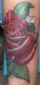 Tattoo of a vibrant red rose with green leaves on a person's arm.
