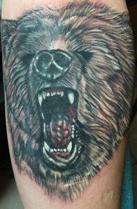 Close-up of a roaring bear face tattoo, with a detailed nose, teeth, and fur, on a limb.
