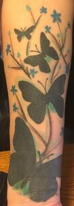 Arm tattoo featuring black butterflies with blue flowers on stems.