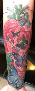 Tattoo of a large red flower with butterflies and small blue flowers on an arm.