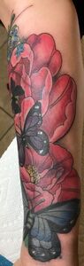 Tattoo of pink flowers and black butterflies on a forearm.