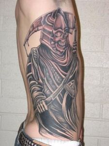 Grim Reaper tattoo on side, holding a scythe. Dark robe, skull face, and brick background.