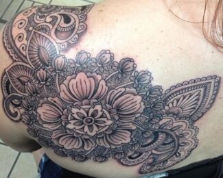 Black ink floral tattoo on a shoulder blade, with detailed patterns and shading.