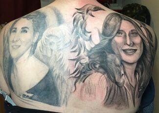 Tattoo on a person's back featuring two portraits and a winged design between them.