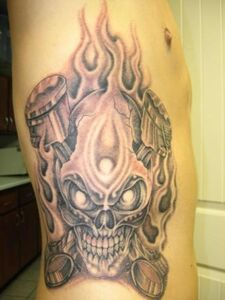 Tattoo of a skull engulfed in flames on a person's side; gray and white shading.