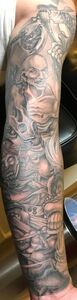 Tattoo of skulls and other figures on a person's arm, in gray scale.