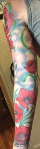Tattoo of red poppies on an arm, with blue sky background, and green stems.