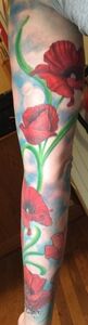 A leg with a tattoo of red poppies with green stems, set against a blue and white cloudy background.