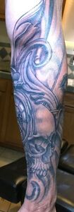 Detailed grayscale tattoo design on a person's lower leg, featuring swirls, a skull, and clock elements.