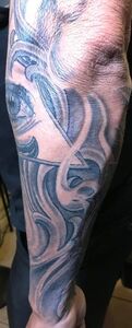 Tattoo of an eye and abstract swirling shapes on an arm. Black and gray shading.