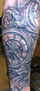 Tattoo of a pocket watch with intricate mechanical details and ornamental swirls on an arm.