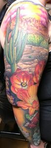 Colorful tattoo of a desert landscape with cactus and vibrant orange flowers on a person's arm.