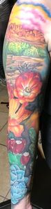 Colorful tattoo of a landscape scene with flowers, lips, and blue geometric shapes on an arm.