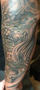 Tattoo of a stylized face wearing a crown, with swirling designs on the arm in grayscale.