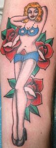 Tattoo of a woman in a blue bikini and high heels, posed between two red roses.