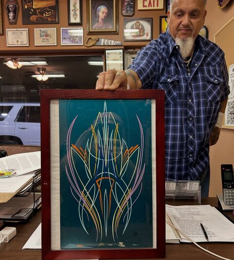 Brent Roman holding a framed pinstripe artwork in the studio