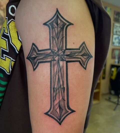 Black and grey ornate cross tattoo on an upper arm