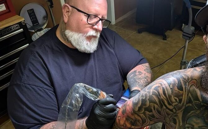 Brent "Taggurr" Roman tattooing a client's arm in the studio